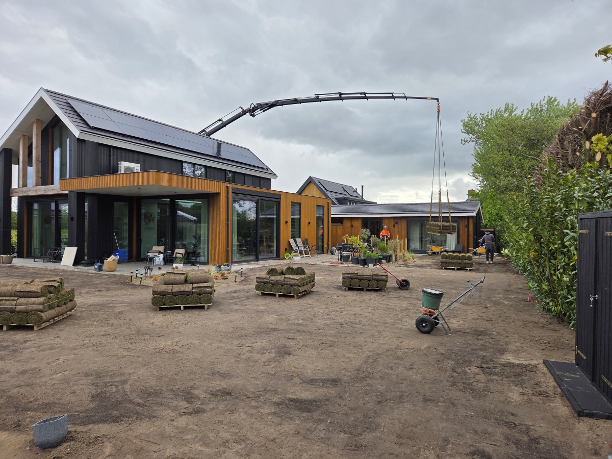 Graszoden worden met een hijskraan over het huis getild voor een gazon van 475 m2 met beregening in Egmond aan den Hoef
